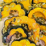 Golden maple roasted acorn squash slices arranged on a parchment-lined baking sheet, glistening with caramelized maple glaze and sprinkled with salted pumpkin seeds.