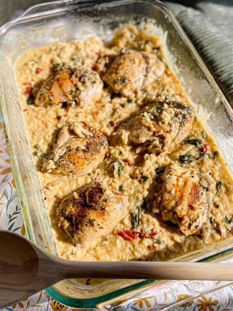 seasoned chicken thighs nestled in creamy rice in a clear baking dish