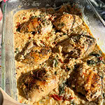seasoned chicken thighs nestled in creamy rice in a clear baking dish