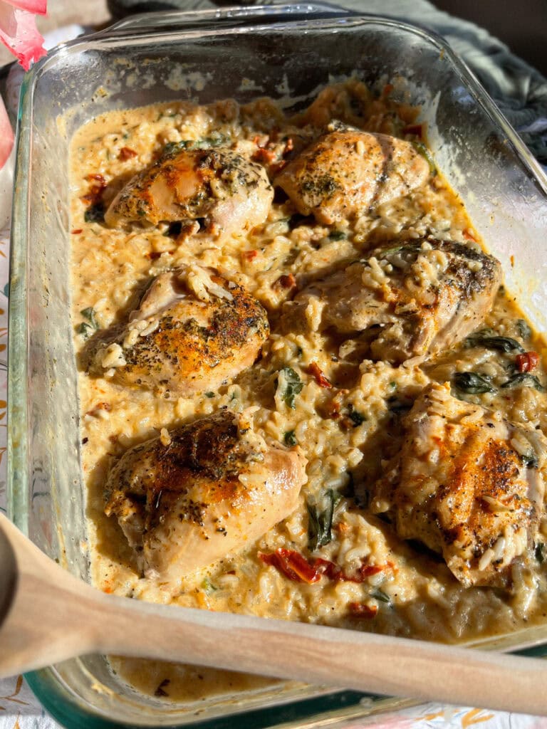 seasoned chicken thighs nestled in creamy rice in a clear baking dish