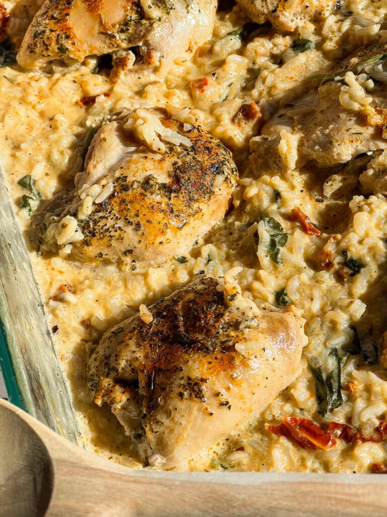 seasoned chicken thighs nestled in creamy rice in a clear baking dish