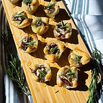 an appetizer of cranberry sauce, brie cheese, rosemary, toasted pecans and honey inside a puff pastry tart lined on a cutting board for serving