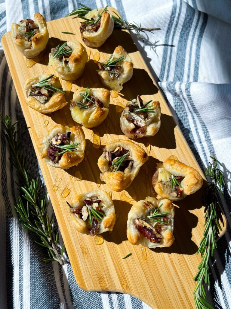 an appetizer of cranberry sauce, brie cheese, rosemary, toasted pecans and honey inside a puff pastry tart lined on a cutting board for serving