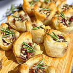an appetizer of cranberry sauce, brie cheese, rosemary, toasted pecans and honey inside a puff pastry tart lined on a cutting board for serving