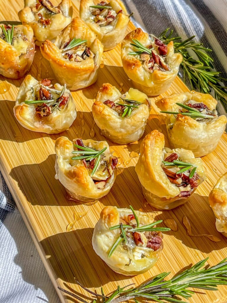 an appetizer of cranberry sauce, brie cheese, rosemary, toasted pecans and honey inside a puff pastry tart lined on a cutting board for serving