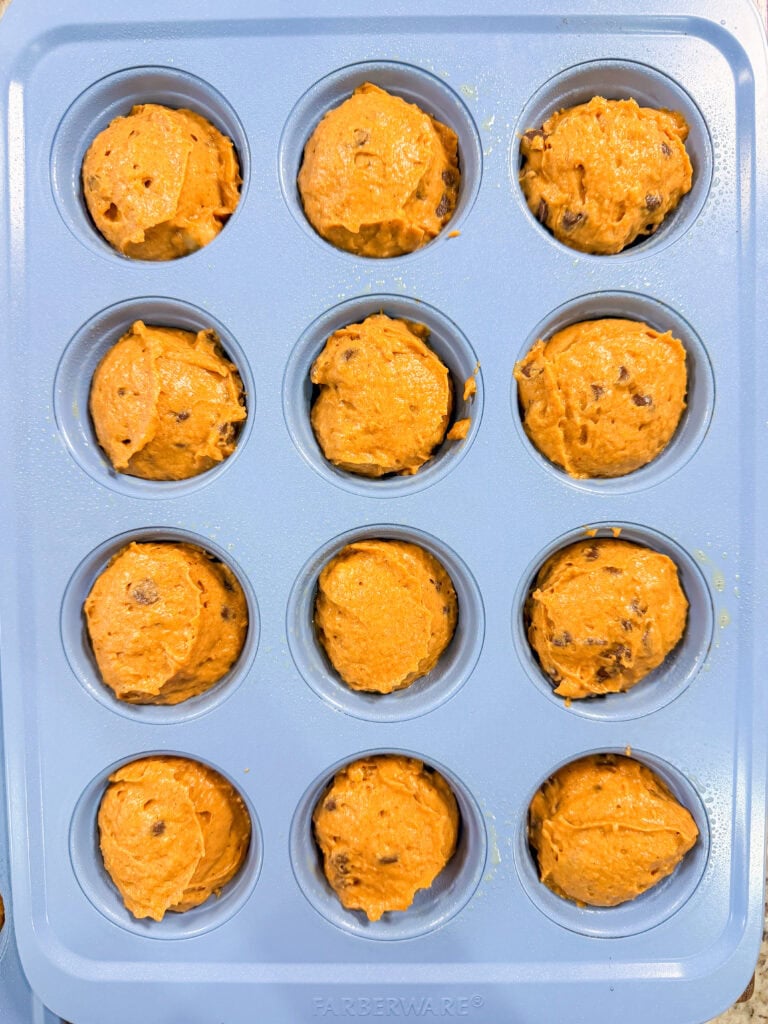 A blue muffin pan filled with unbaked Pumpkin Chocolate Chip Muffins batter, each cup portioned with dough, ready to be baked.