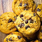 A close-up of Pumpkin Chocolate Chip Muffins arranged on a wooden surface. The muffins are golden-brown with visible chocolate chips.