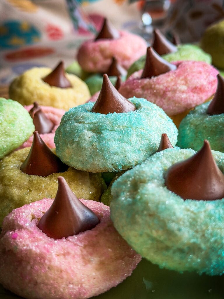 Colorful sugar cookies with pastel pink, blue, and yellow coatings, each topped with a milk chocolate Hershey’s Kiss, are stacked closely together in a bright, festive arrangement—an ideal treat to pair with Overnight Hashbrown Breakfast Casserole.