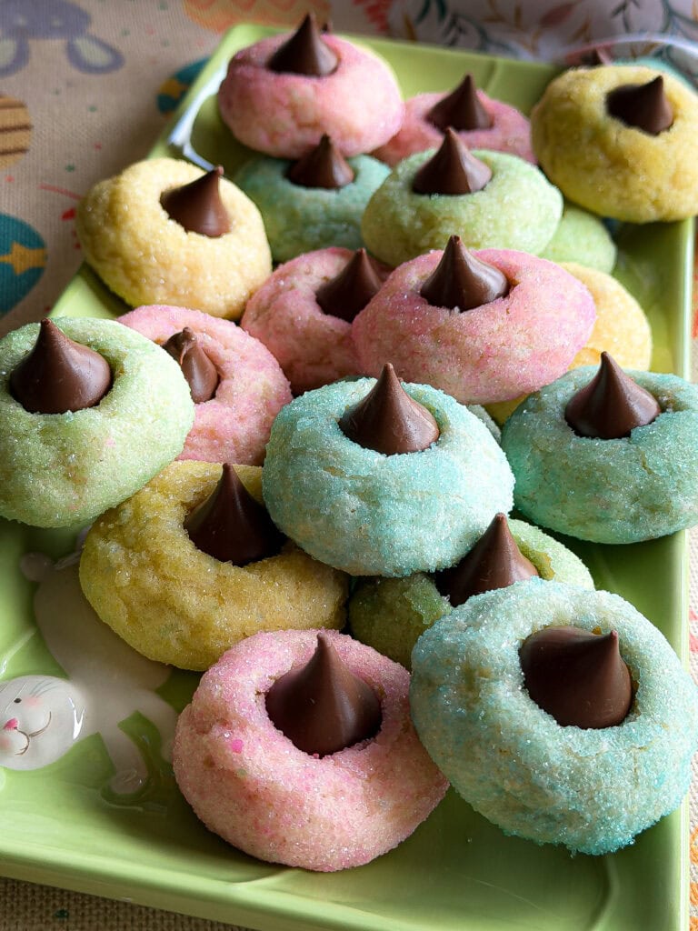 Pastel-colored sugar cookies topped with Hershey’s Kisses on a green plate. These cookies, coated in pink, blue, yellow, and green sparkling sugar, are perfect for Easter or spring—just like an Overnight Hashbrown Breakfast Casserole for brunch!.