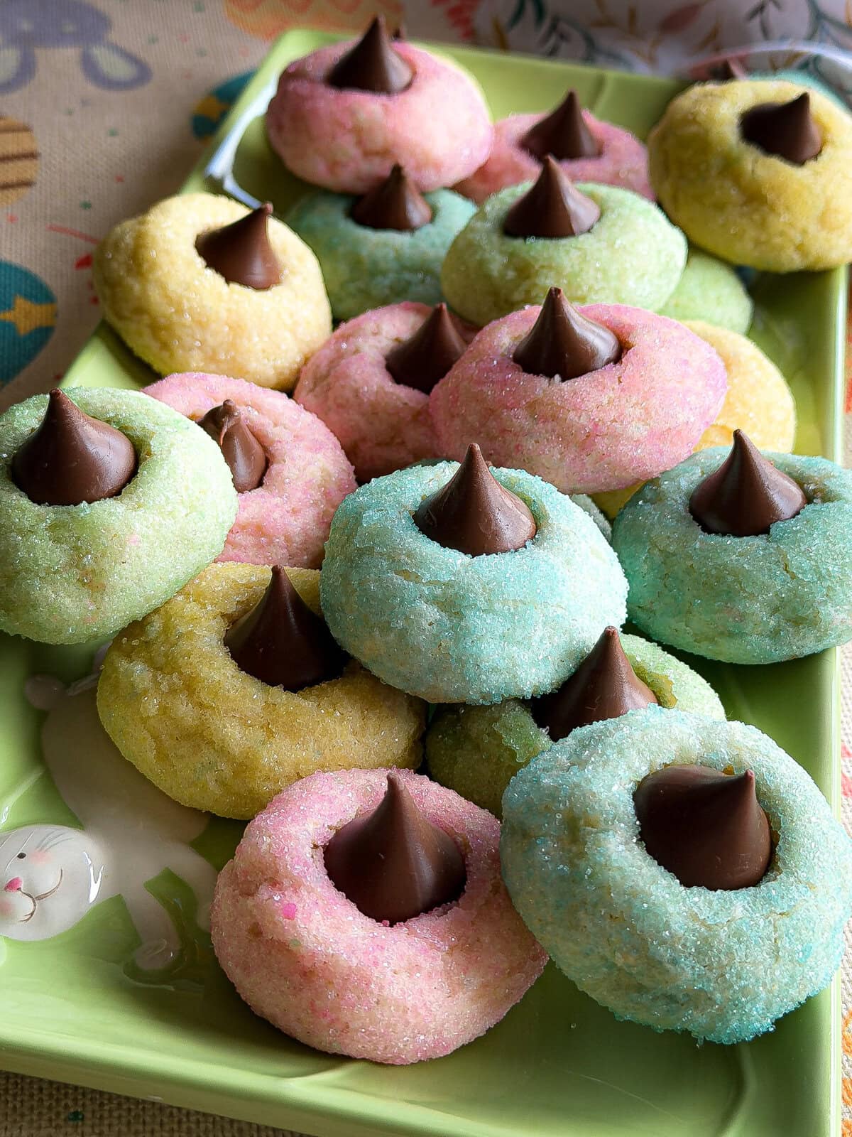 Pastel-colored sugar cookies topped with Hershey’s Kisses on a green plate. These cookies, coated in pink, blue, yellow, and green sparkling sugar, are perfect for Easter or spring—just like an Overnight Hashbrown Breakfast Casserole for brunch!.
