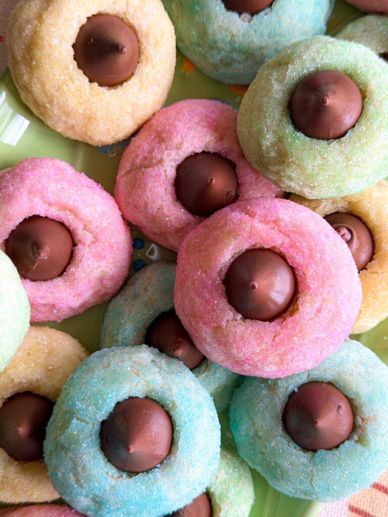 Colorful sugar-coated cookies in pastel shades of pink, blue, green, and yellow, each topped with a single chocolate candy and arranged closely together on a plate—perfect alongside an Overnight Hashbrown Breakfast Casserole for a festive brunch spread.