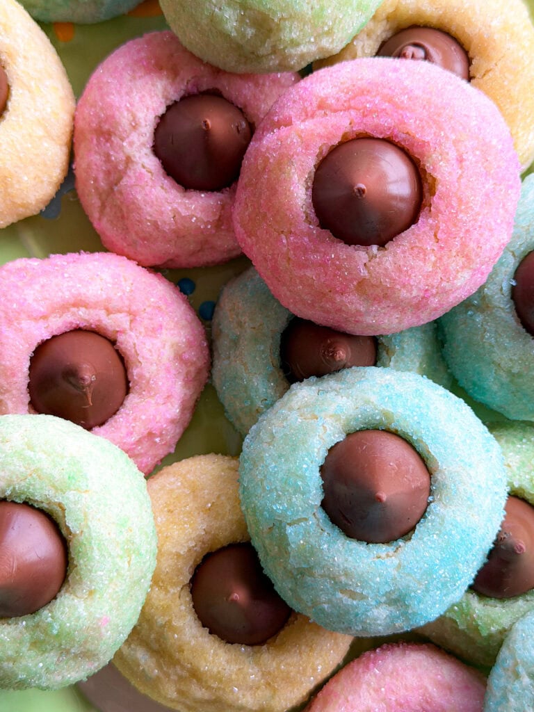 A close-up of colorful sugar cookies in pastel pink, blue, yellow, and green, each topped with a round chocolate candy in the center—perfect alongside an Overnight Hashbrown Breakfast Casserole for a festive brunch spread.