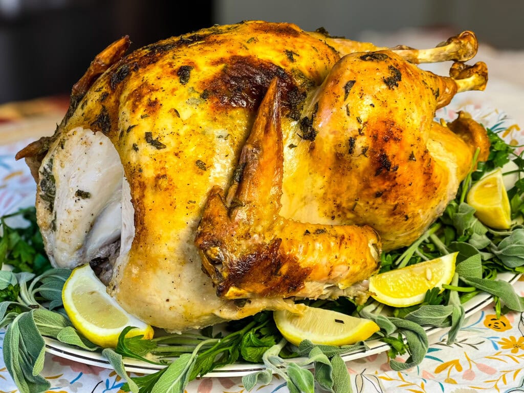 a whole roasted turkey with fresh herbs underneath on a serving platter