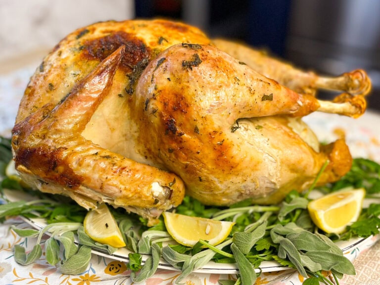 a whole roasted turkey with fresh herbs underneath on a serving platter