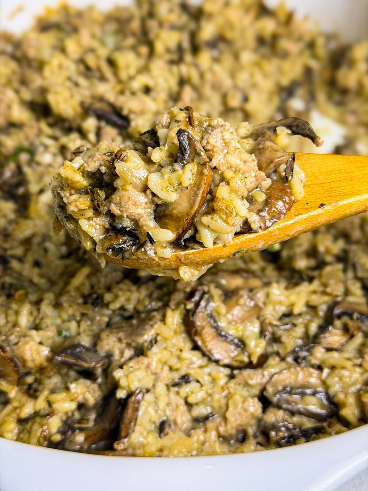 wild rice casserole with Italian sausage and mushrooms on a spoon over a baking dish