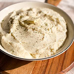 creamy mashed cauliflower in a serving bowl with a pat of butter and black pepper