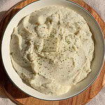 creamy mashed cauliflower in a serving bowl with a pat of butter and black pepper