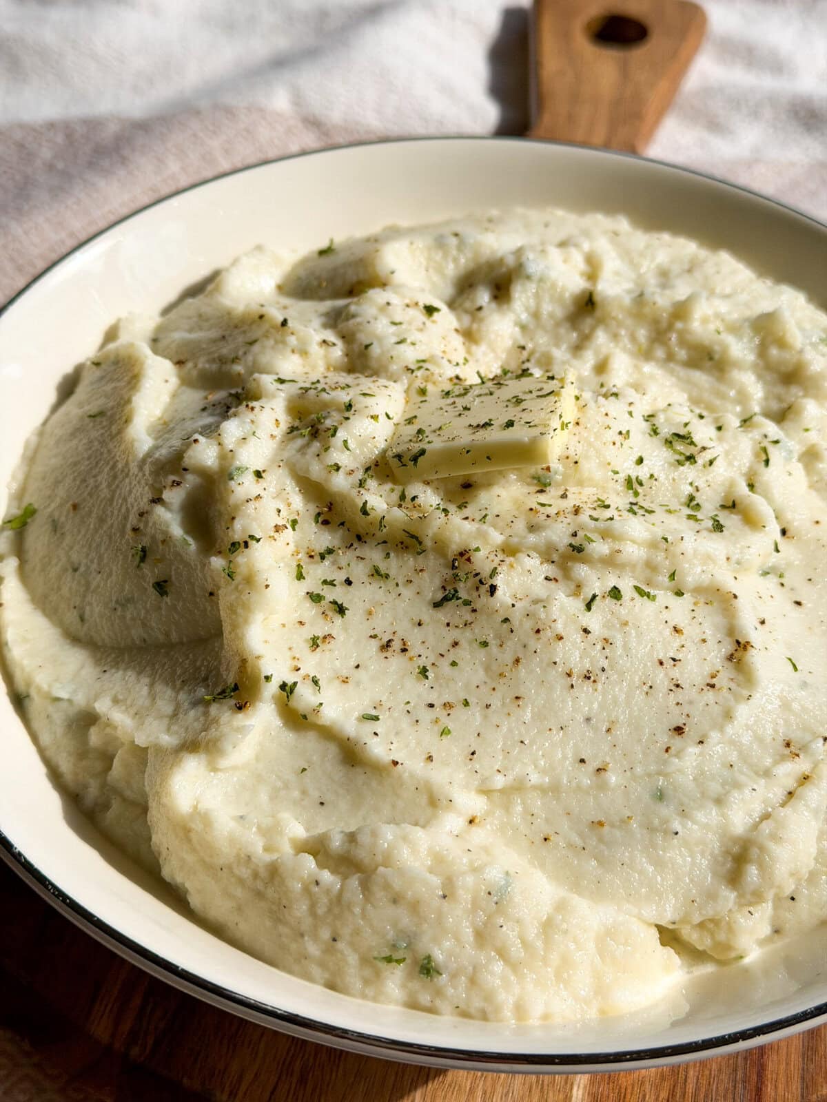 creamy mashed cauliflower in a serving bowl with a pat of butter and black pepper