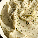 creamy mashed cauliflower in a serving bowl with a pat of butter and black pepper