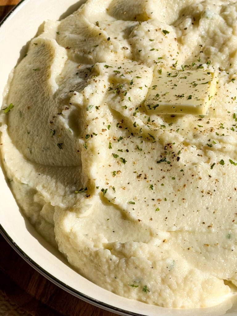 creamy mashed cauliflower in a serving bowl with a pat of butter and black pepper