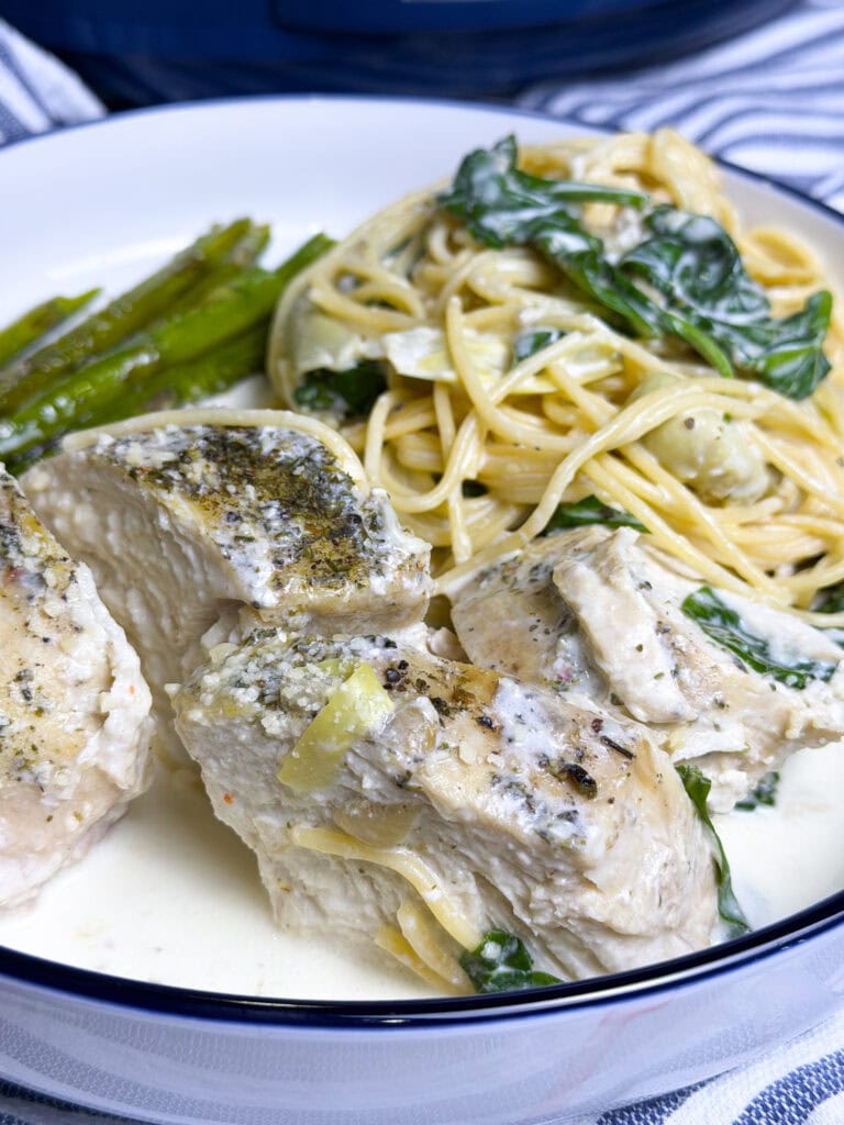 sliced chicken cooked in a crock pot with a cream cheese spinach sauce spooned over and a side of spaghetti