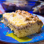 A slice of breakfast casserole made with hashbrowns, sausage, eggs, and cheese on a blue plate with the blue casserole serving dish in the background