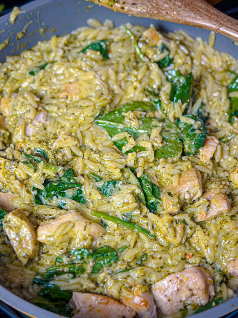 creamy orzo pasta with spinach and pieces or chicken in a sautee pan