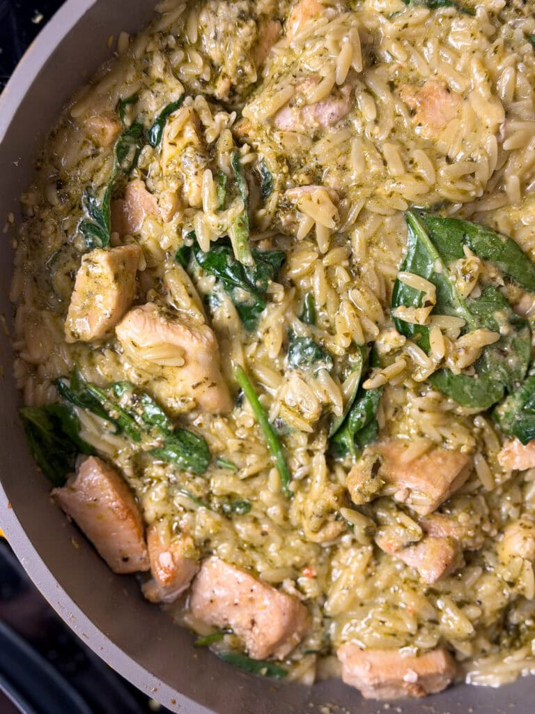 creamy orzo pasta with spinach and pieces or chicken in a sautee pan
