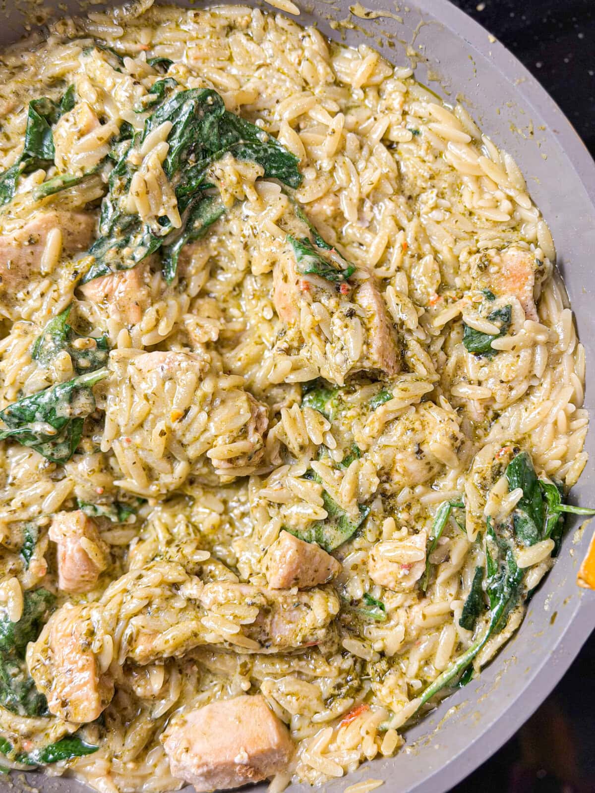 creamy orzo pasta with spinach and pieces or chicken in a sautee pan