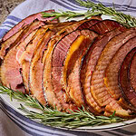 spiral slices of ham made with cherry coke glaze laid out on a white serving platter with sprigs of rosemary