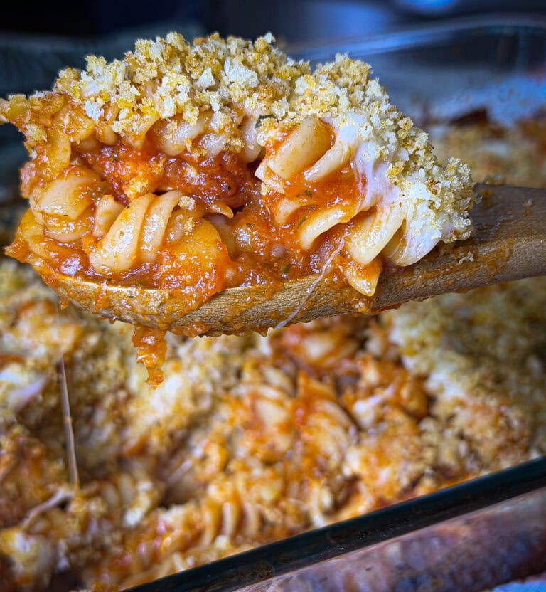 A golden, cheesy baked chicken Parmesan casserole in a large white dish, topped with crispy seasoned breadcrumbs and melted mozzarella, with tender pasta and pieces of chicken visible underneath.