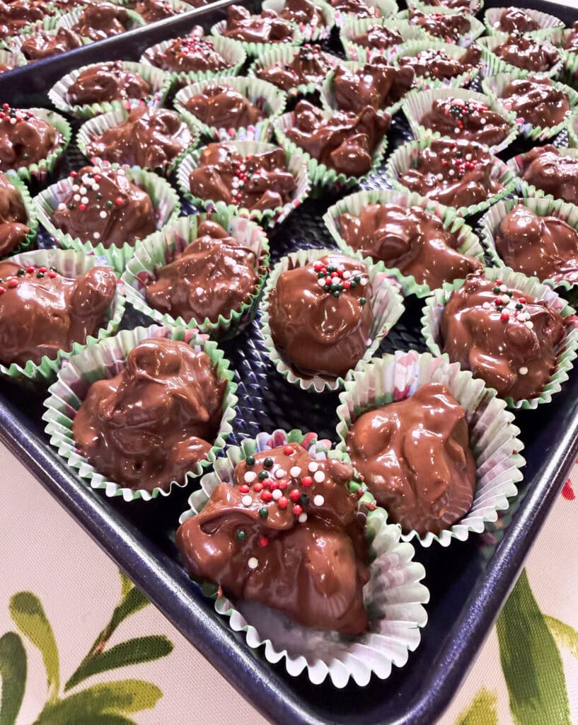 chocolate covered mixed nuts with pretzels scooped into a green mini muffin liner with red, green, and white sprinkles all made in the slow cooker
