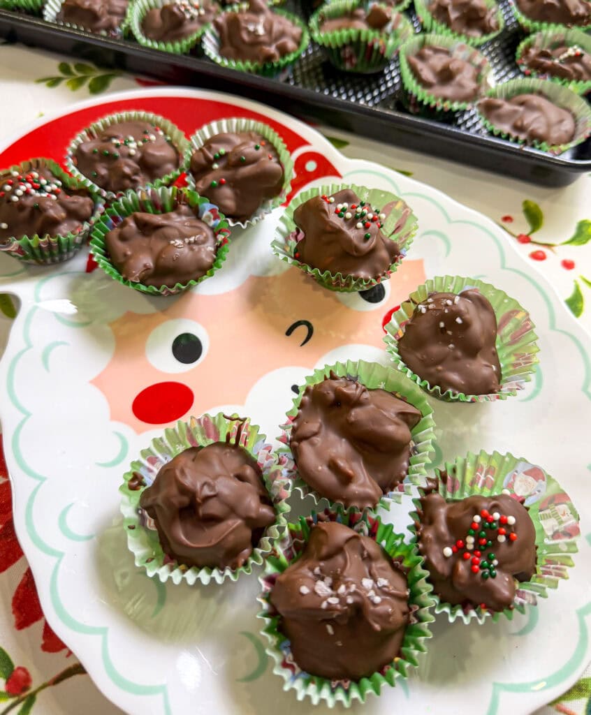 chocolate covered mixed nuts with pretzels scooped into a green mini muffin liner with red, green, and white sprinkles all made in the slow cooker
