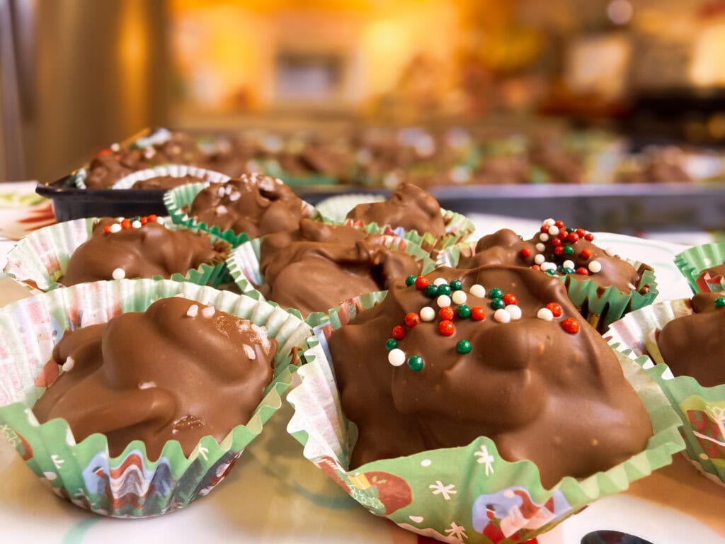 chocolate covered mixed nuts with pretzels scooped into a green mini muffin liner with red, green, and white sprinkles all made in the slow cooker