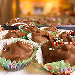 chocolate covered mixed nuts with pretzels scooped into a green mini muffin liner with red, green, and white sprinkles all made in the slow cooker