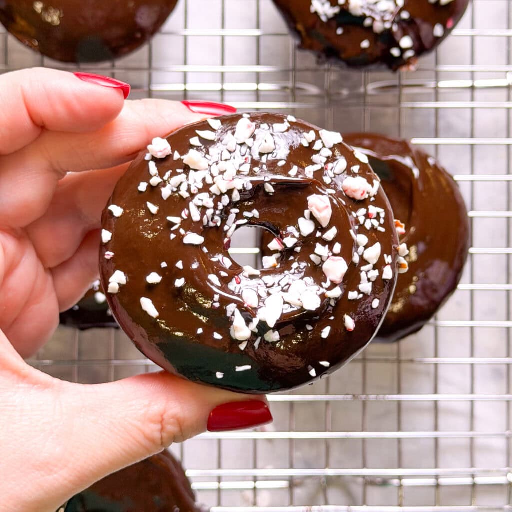 Close-up of baked chocolate peppermint donuts with smooth chocolate ganache and festive crushed candy cane pieces.