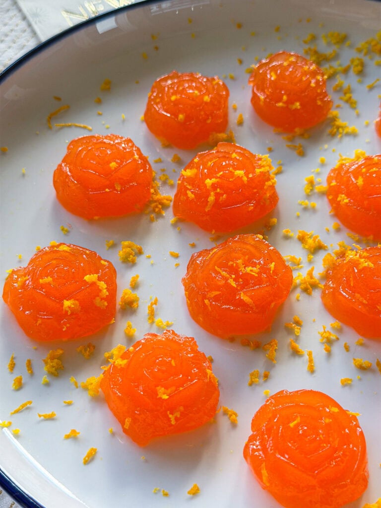 Aperol spritz Jell-O shots garnished with orange zest on a serving tray.