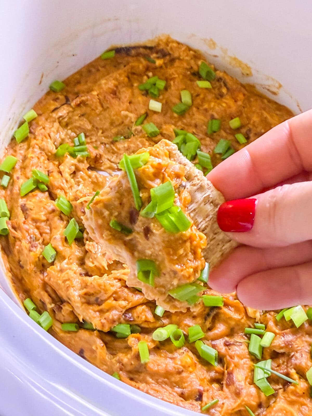 shredded chicken cream cheese sweet chili sauce dip in a white crock pot topped with sliced green onions