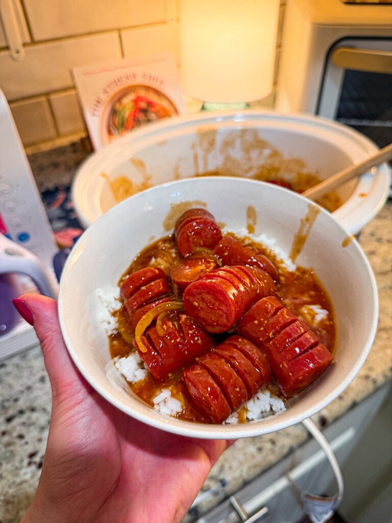 kielbasa cut hasselback style in a sweet and savory sauce over rice with onion slices in a bowl