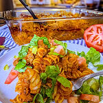 One-dish baked cheeseburger pasta served on a plate with melted cheddar cheese, diced pickles, shredded lettuce, and chopped tomatoes.
