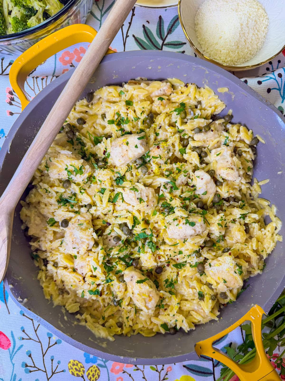 creamy chicken piccata with orzo being served from a yellow skillet with a wooden spoon resting on the skillet
