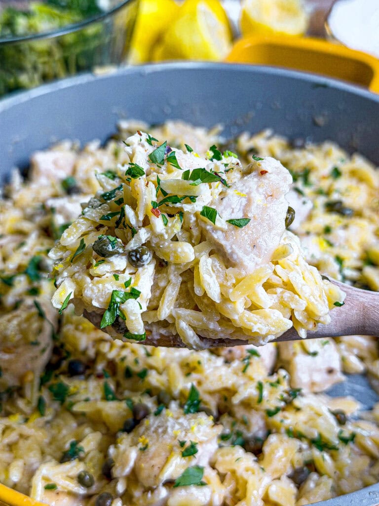 close up of chicken piccata with orzo on a wooden spoon