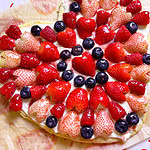 Heart shaped sugar cookie fruit pizza topped with cream cheese frosting, strawberries, blueberries, raspberries, and a glossy jam glaze for Valentine’s Day.