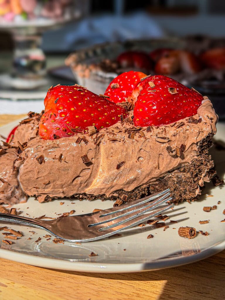 slice of no bake chocolate pudding pie with sliced strawberries on top and shaved chocolate