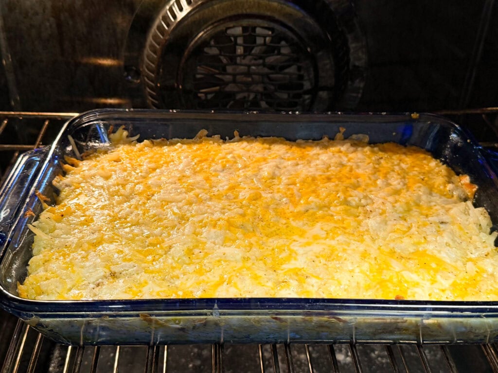 A glass baking dish filled with a cheesy casserole is shown baking in an oven. The casserole has a golden brown, melted cheese topping.