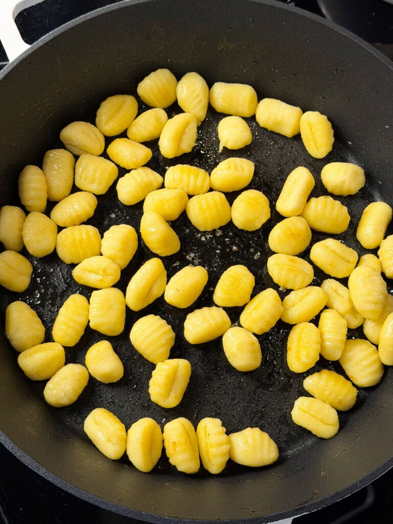 A close-up of uncooked gnocchi scattered in a black frying pan, ready to be cooked.