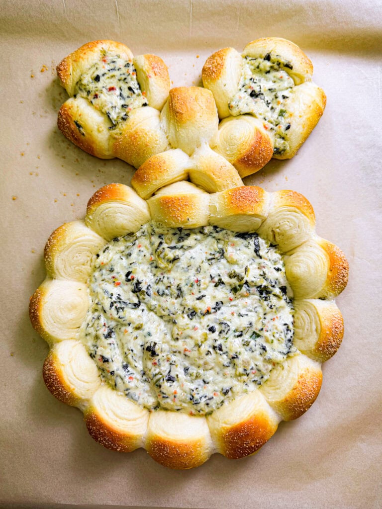 A bread bowl shaped like a bunny, filled with creamy spinach and cheese dip, sits on parchment paper—one of the cutest Easy Easter Treat Ideas. The round body holds the dip, while two smaller rolls form the head and ears.