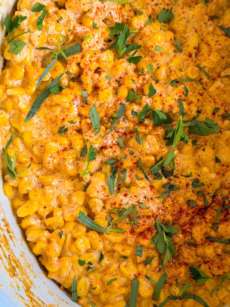 Creamy corn mixed with herbs and sprinkled with paprika and chopped parsley, creating a colorful and appetizing dish.