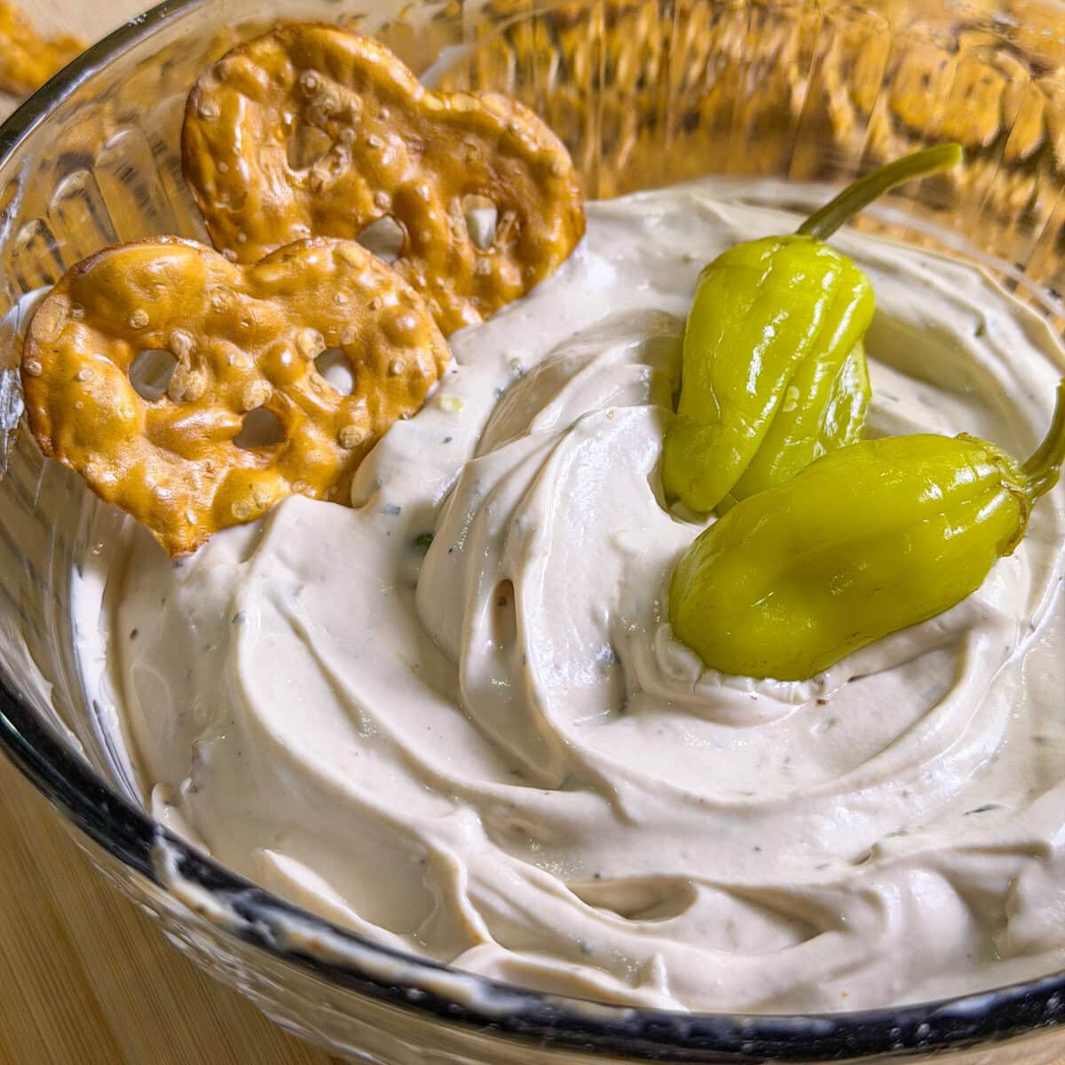 A glass bowl of creamy dip topped with two green peppers, with two heart-shaped pretzel crisps partially dipped into the mixture.