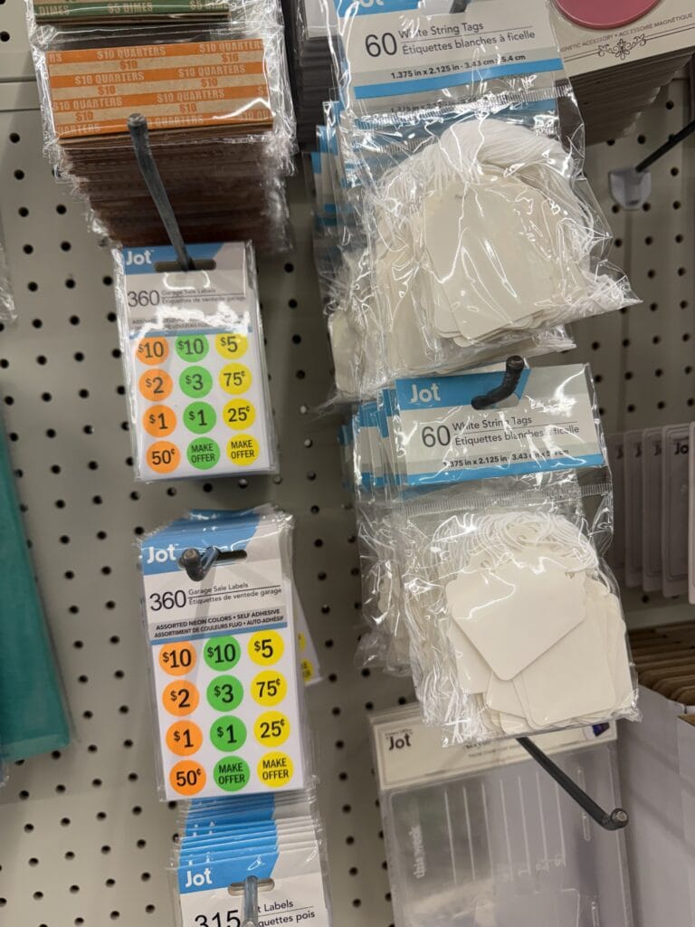 Packages of Jot brand price stickers and string tags hang on a store display. Price stickers are in various colors and denominations, while white string tags are bundled in clear plastic packaging.